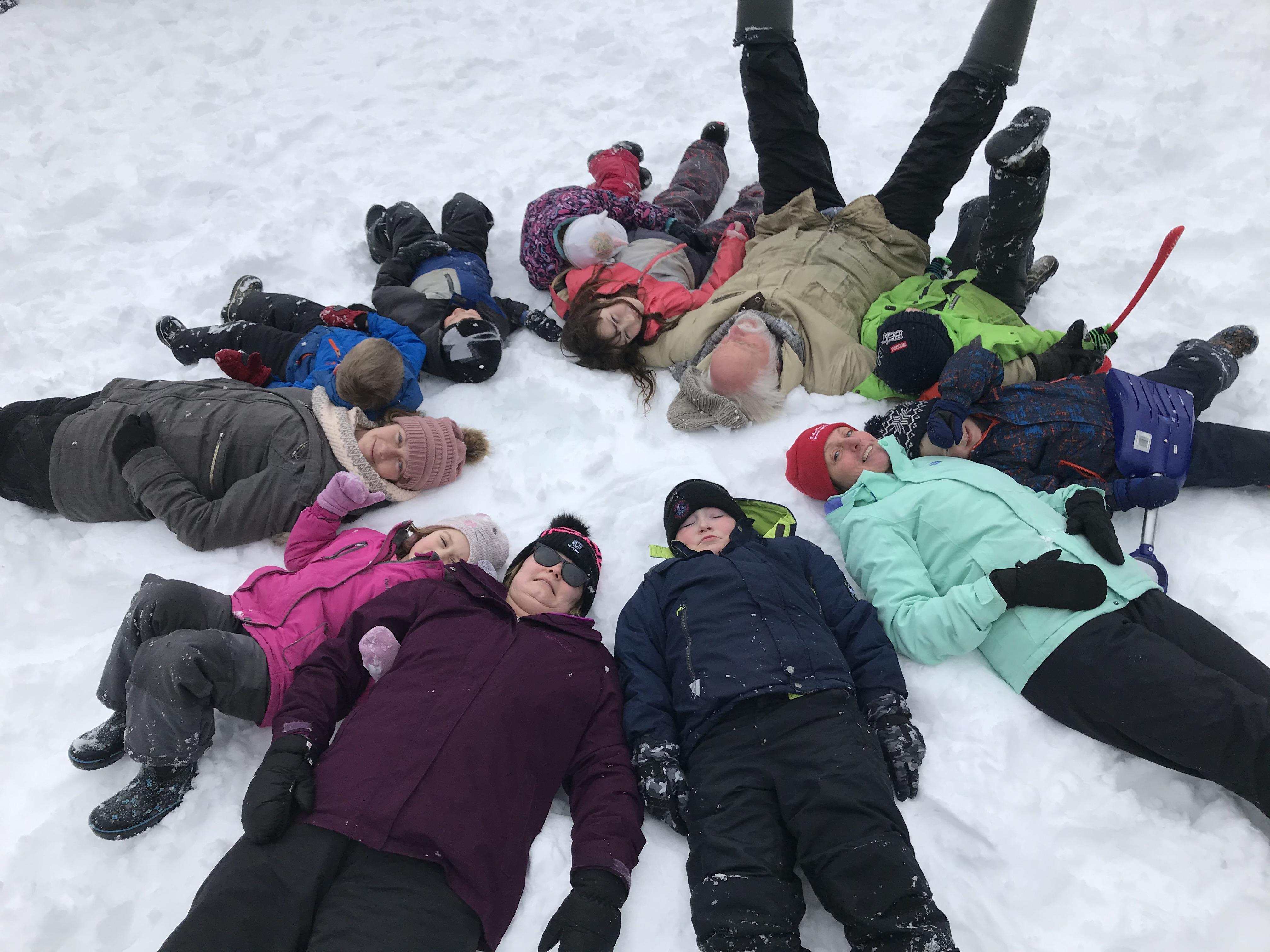 A group of children and adults lie in a circle in the snow.